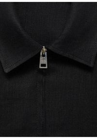 Black collared shirt featuring a silver metallic zipper at the neck, made from textured fabric with a subtle weave pattern.