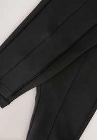 Black athletic pants featuring a smooth texture, tapered legs, and distinct seams along the sides for added definition.