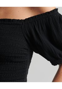 Sort off-the-shoulder top med tekstureret smocking og puffede ærmer, med en samlet elastisk halslinning og blødt, flydende stof.