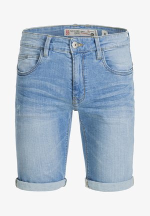 Chemise blanche en lin avec boutons, short en denim bleu clair à ourlet retroussé, baskets blanches. Tenue décontractée avec une coupe ample et des couleurs claires.