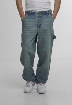 Light blue loose-fitting denim jeans with a faded texture, front pockets, and a side loop. Paired with white sneakers for contrast.