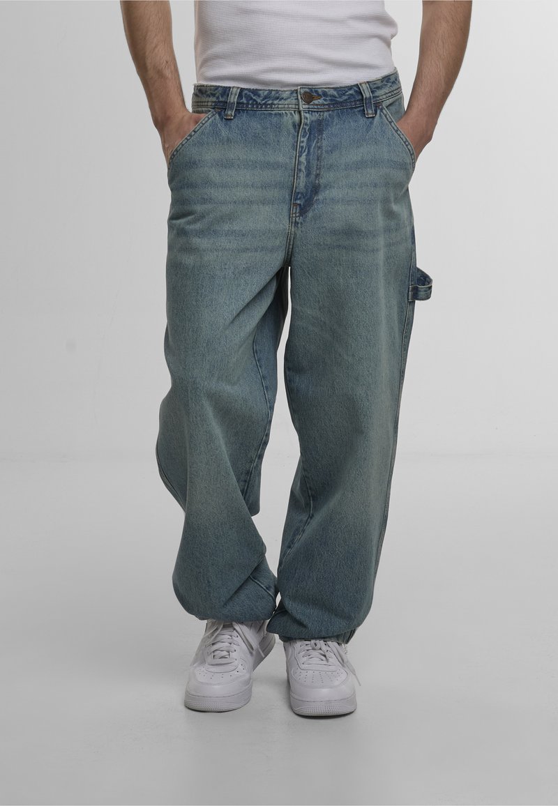 Light blue loose-fitting denim jeans with a faded texture, front pockets, and a side loop. Paired with white sneakers for contrast.