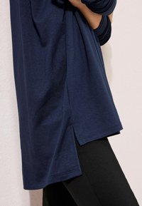 Dugorukava majica tamnoplave boje od mekanog materijala sa bočnim prorezima, u ležernom kroju. Kombinirana s crnim uskim hlačama.