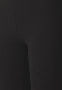Čierne legíny s hladkým, pružným materiálom. Detailný pohľad ukazuje elegantný dizajn a priliehavý strih, bez viditeľných vzorov alebo akcentov.
