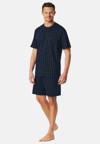 Camiseta azul marino con estampado geométrico en blanco, mangas cortas, combinada con pantalones cortos azul marino lisos. Material de algodón, ajuste informal.