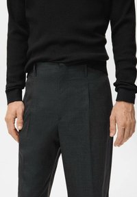 Dark gray tailored trousers with a subtle check pattern and straight cut. Complemented by a black ribbed knit sweater.