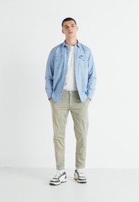 Lys blå denimskjorte over en hvit T-skjorte, kombinert med lysegrønne bukser og svart-hvite sneakers. Enkel design, uformell passform.