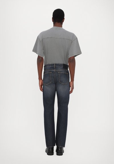 Grå kortärmad skjorta i kombination med mörkblå raka jeans. Jeansen har två bakfickor och en subtil sömdetalj. Svarta skor fulländar looken.