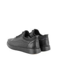 Zwarte lederen sneakers met een strak ontwerp, ronde neus, gestructureerd oppervlak en een gewatteerde kraag. Voorzien van een rubberen zool met horizontale groeven.