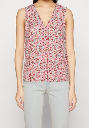 Ærmeløs V-hals bluse med et flerfarvet lille blomstermønster, båret med lyseblå jeans på en stående person.