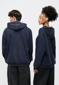 Oversized navy hoodie in soft cotton, featuring a drawstring hood, ribbed cuffs, and a kangaroo pocket, worn with black jeans.