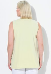 Top senza maniche in cotone giallo chiaro con orlo arrotondato. Texture liscia, design semplice e senza motivi o dettagli hardware visibili.