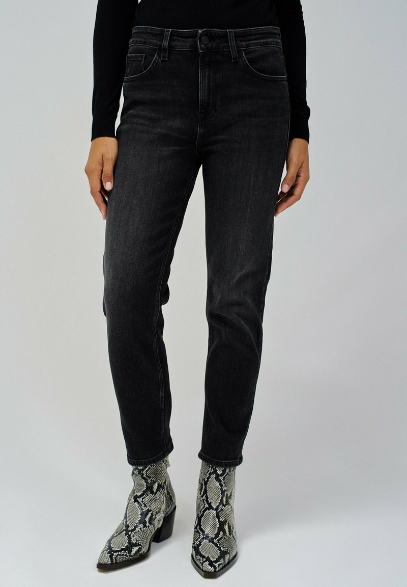 Jeans en denim noir avec une coupe slim, cinq poches et une taille mi-haute, associés à des bottes chevilles à imprimé serpent et un haut noir à manches longues.