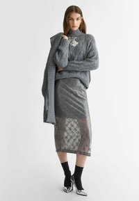 Maglione grigio lavorato a maglia con motivo testurizzato, abbinato a una gonna a matita grigia in paillettes con sovrapposizione trasparente a motivo. Calze nere e tacchi argentati.