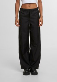 Zwarte wijde broek met een elastische tailleband, trekkoorddetails en een gladde stoftextuur. Geen zichtbare patronen of accenten.