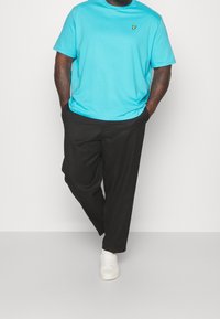 Lichtblauwe katoenen t-shirt met een klein geel logo, gecombineerd met zwarte broeken en witte sneakers. Deoutfit heeft een ontspannen pasvorm.