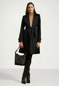 Μαύρο παλτό με διπλή σειρά κουμπιών, ζώνη στην μέση και επωμίδες στον ώμο. Συνδυασμένο με μία υφαντή μαύρη τσάντα και μποτάκια μέχρι το γόνατο.