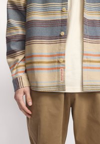Gestreepte overhemden in blauw, beige en oranje, gemaakt van zacht materiaal, gecombineerd met lichtbruine pantalons; beschikt over logo-detail op het shirt.