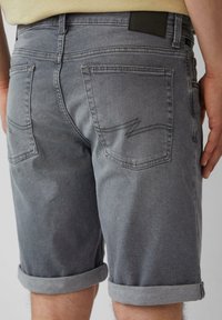 Graue Jeans-Shorts mit umgeschlagenen Säumen, ausgestattet mit Gesäßtaschen und subtilen Stickdetails. Glatte Textur und normale Passform.