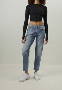 Ljusblå, avslappnade jeans med blekt utseende, matchade med en svart crop top med långa ärmar och vita sneakers. Mjukt tyg, avslappnad design.