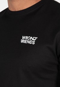 Sort bomulds T-shirt med rund halsudskæring og korte ærmer, der har et hvidt "WRONG FRIENDS" logo printet på venstre bryst.