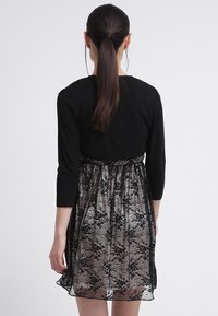 Musta paita, jossa on kolme neljänneskäden hihaa, sifonkihame mustalla pitsikerroksella, joustava vyötärö, polvipituinen malli ja kerrosmainen rakenne.