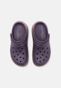Sabots violets avec un design perforé et une sangle arrière réglable, dotés d'une semelle intérieure rembourrée et d'un accent marron sur la semelle.