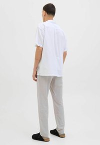 Chemise blanche à manches courtes avec une coupe décontractée, associée à un pantalon gris clair et des chaussures noires à enfiler. Design simple et minimaliste.