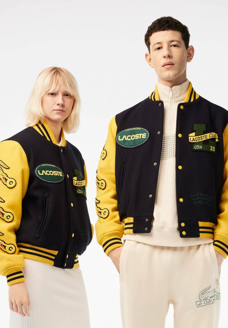 Veste varsity en laine navy et jaune, avec des motifs en patch et des broderies, des poignets côtelés, des boutons-pression et deux poches avant.