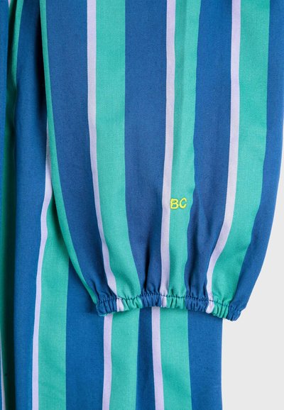 Tessuto rigato con ampie linee blu e verdi, caratterizzato da un polsino arricciato e un piccolo ricamo giallo "BC". Texture in cotone.