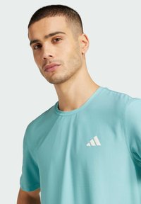 Camiseta deportiva de color azul claro con tejido texturizado y mangas cortas, que presenta un logo triangular blanco en el lado izquierdo del pecho.