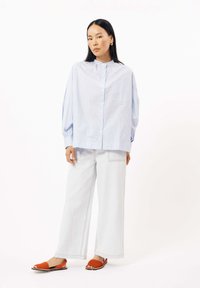 Blauw-wit gestreepte button-up shirt met een patch pocket, gecombineerd met wijde licht denim broek en oranje instapsandalen.