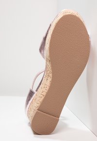 Sandale compensée avec plateforme effet liège et semelle beige texturée, présentant des brides supérieures métalliques roses et un design à bout ouvert.