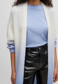 Lång, öppen cardigan i en vit till ljusblå gradientstickning, lager-på-lager över en ljusbl�å skjorta, kombinerat med högmidjade svarta fauxläderbyxor.