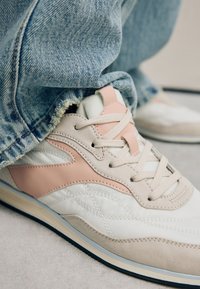 Sneaker med hvidt, beige og pastelrosa farveskema, tekstureret materiale, snøredesign og en kontrasterende sål.