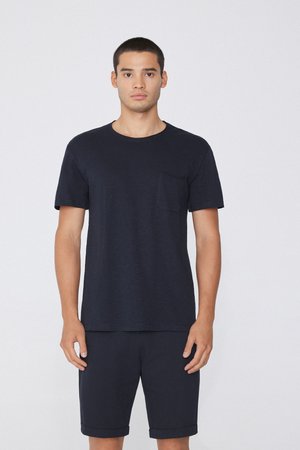 Junger Mann, der nach vorne steht, trägt ein einfaches schwarzes Kurzarm-T-Shirt mit Tasche und passende schwarze Shorts.