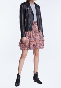 Veste en cuir noir de biker associée à un t-shirt gris clair et à une mini-jupe à fleurs multicolores. Des bottes noires à la cheville complètent le look.