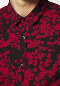 Zwarte overhemden met een rood bloemenpatroon, met een spitse kraag en zwarte knopen, gemaakt van een textuurstof.