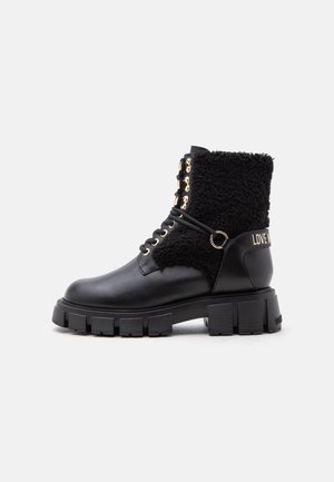 Black lace-up boot with chunky sole, textured fabric upper, gold eyelets, and "LOVE" text on the heel tab.
