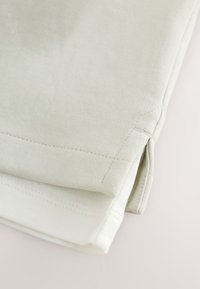 Gros plan de l'ourlet et de la fente latérale sur un vêtement en maille beige clair.