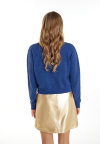 Maglione blu fluffy con maniche lunghe abbinato a una mini gonna dorata lucente, che presenta una texture liscia e un orlo curvo.