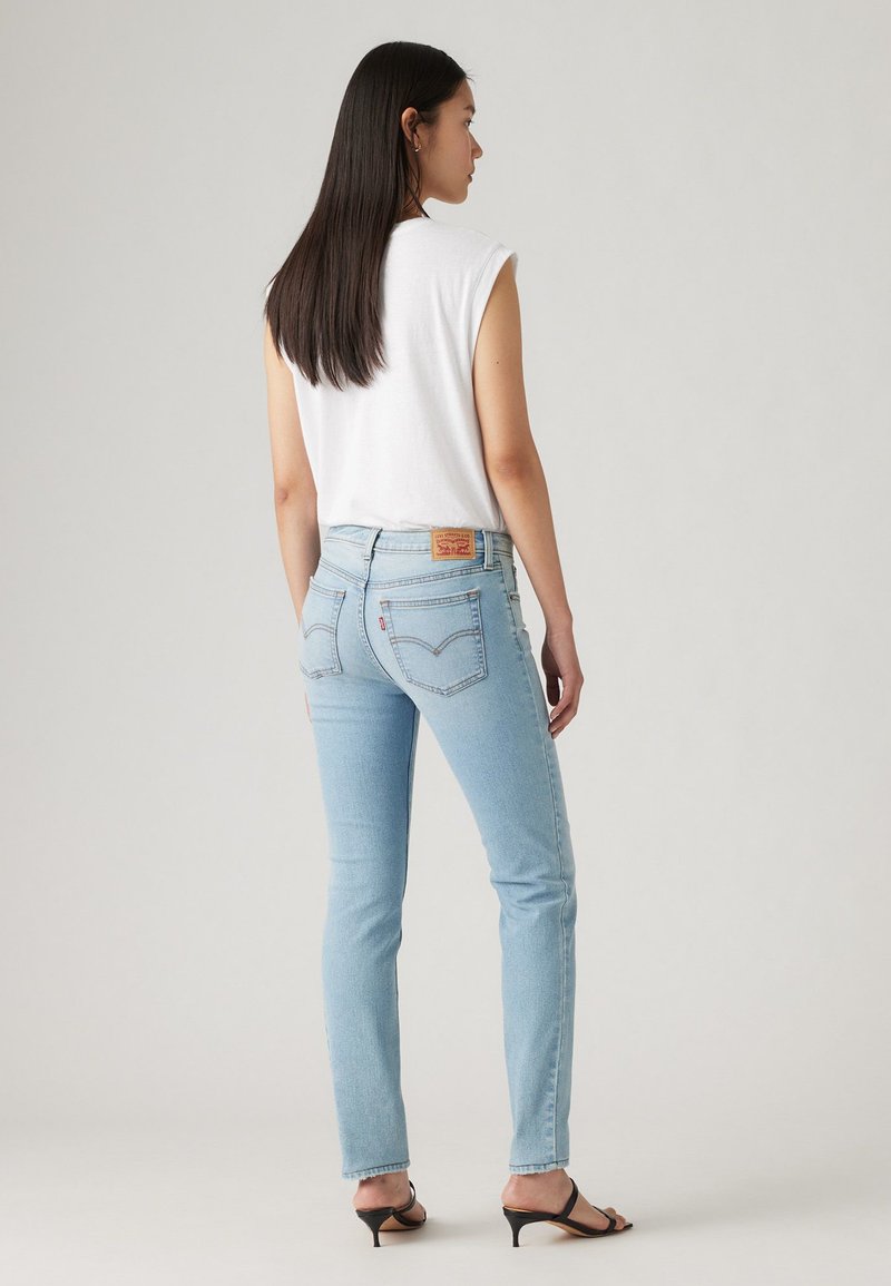 Jean en denim bleu clair avec une coupe droite et des coutures classiques. Porté avec un haut sans manches blanc et des sandales noires à talons.