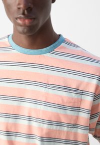 Stribet kortærmet t-shirt med farverne laks-rosa, mintgrøn og marineblå, med rund halsudskæring og en brystlomme.