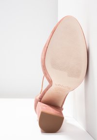 Chaussure à talons hauts en suède rose avec une semelle texturée, dotée d'un talon épais et d'un design ouvert. La tige présente une texture lisse et douce ainsi que des lignes élégantes.