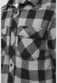 Svart og grå rutete flanellskjorte med knappelukking foran, to brystlommer med klaffer, og et mykt, teksturert stoff.