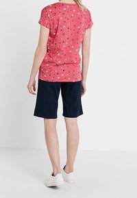Camiseta corta de manga corta con estampado floral rojo combinada con pantalones cortos azul marino. El material parece suave; la camiseta presenta pequeños patrones de flores blancas y azules.