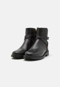 Bottines en cuir noir avec un bout arrondi, une sangle décorative et des détails en métal doré, et un petit talon carré. Texture lisse.