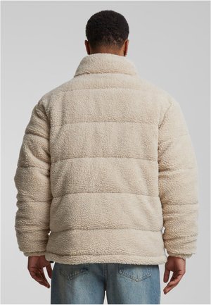 Beige fleecetröja med hög krage, texturerad yta, kviltat mönster och långa ärmar, visad från baksidan.