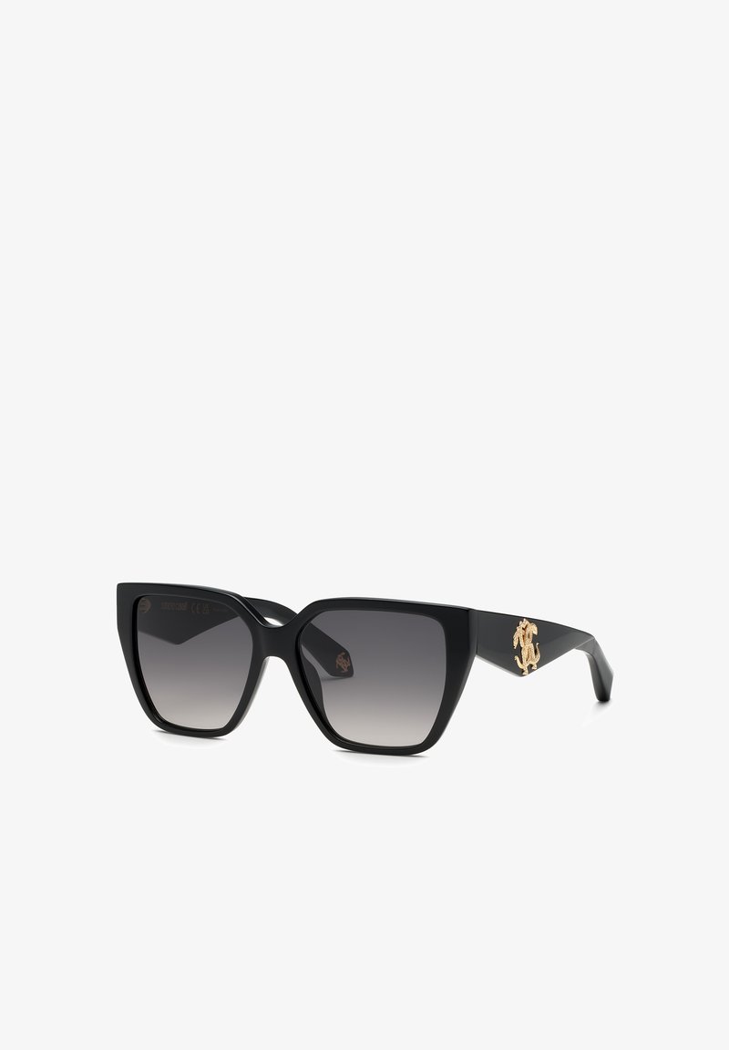 Lunettes de soleil noires oversize œil de chat avec verres dégradés foncés et logo décoratif doré sur les branches sur fond blanc.