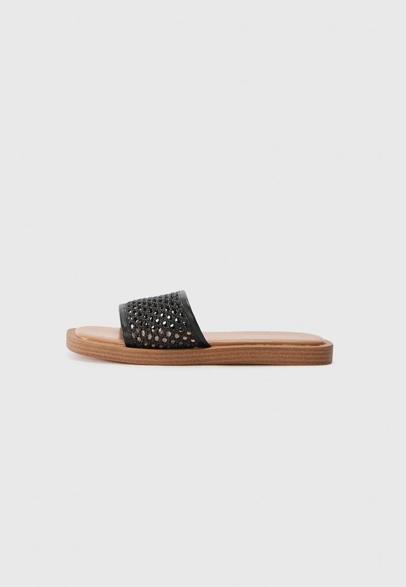 Svart sandale med flatt design som har en vevd overdel, glatt lærfotseng og tresåle.